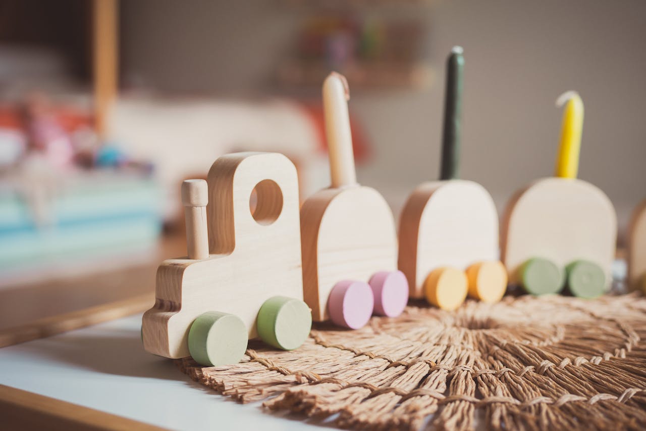 A close-up of a colorful wooden toy train set on a woven mat in a cozy room.